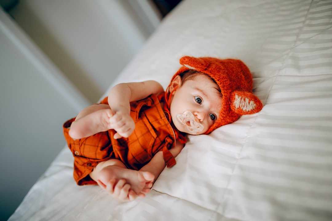 baby in orange knit cap lying on white bed E6f ln7TjRg jpg